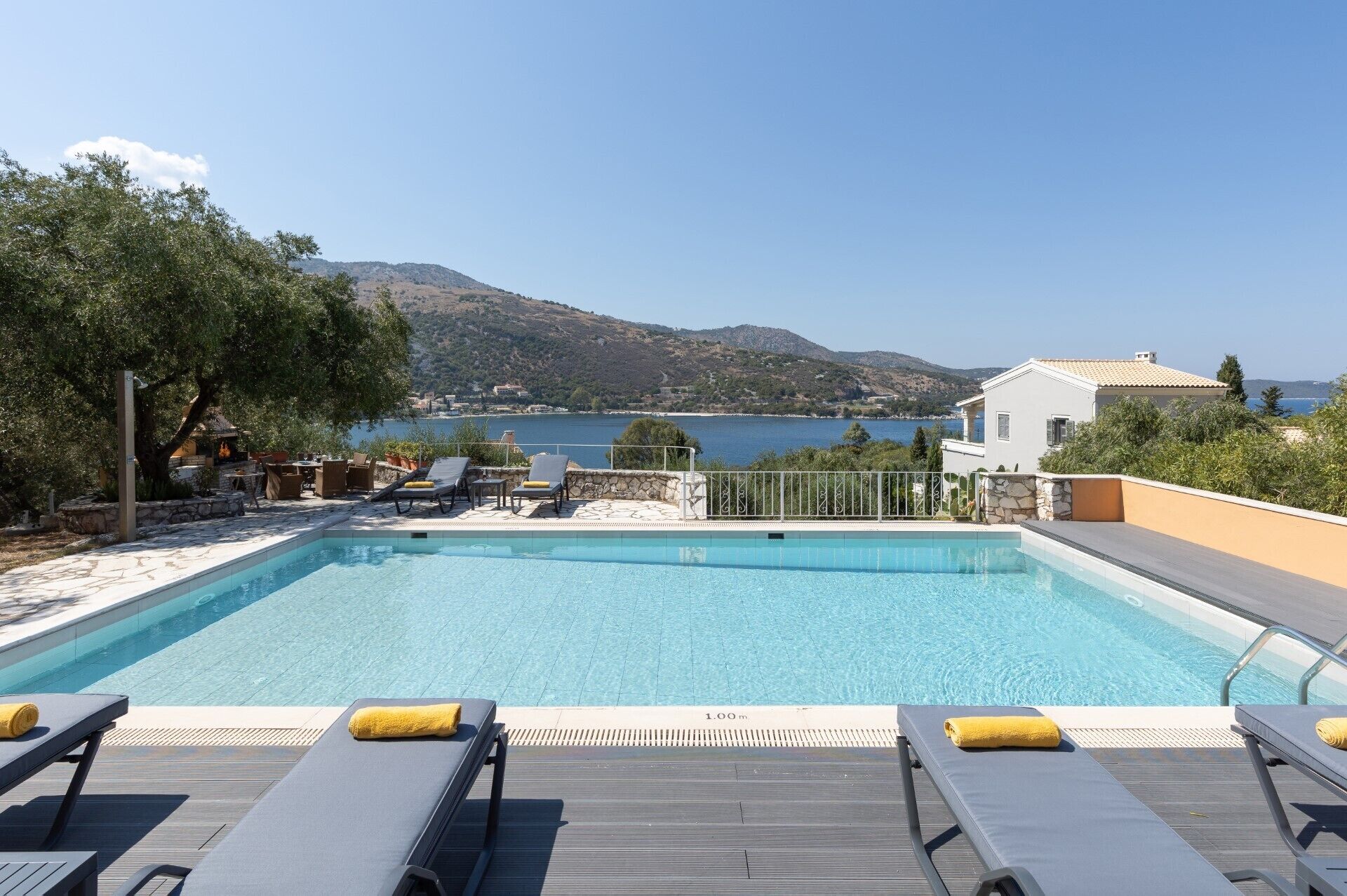 A swimming pool with lounge chairs and a view of the sea and hills.