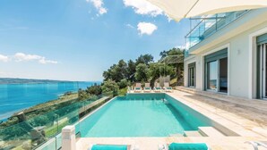 Ein moderner Poolbereich mit klarem, blauem Wasser, einer Glasbrüstung und Blick aufs Meer.