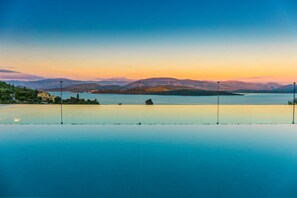 Una piscina infinita tranquila con vistas despejadas a una costa lejana, una cadena montañosa y un atardecer.