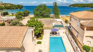 Area piscina con vista aperta sul mare, circondata da edifici con tetti in tegole e un giardino.