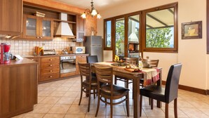 A kitchen with wooden cabinets, a built-in oven, a microwave, and a dining area with a table and chairs. - Villa Firefly by Villa Plus (Άγιος Στέφανος)