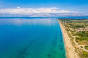 An aerial view of a coastal area with a beach, a road, and scattered buildings. - Villa Finikas by Villa Plus (Corfu)
