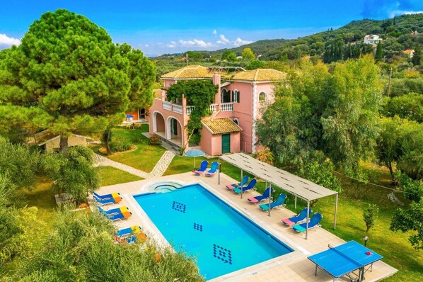 A villa with a swimming pool, outdoor seating, and a garden.