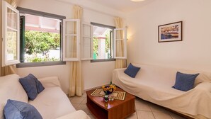 A room with two white sofas, one with blue cushions, a wooden coffee table with a vase of flowers, and a framed picture on the wall. - Villa Foula by Villa Plus (Άγιος Στέφανος)