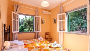 A bedroom with two beds, a chair, a lamp, and two windows with curtains. - Villa Foula by Villa Plus (Άγιος Στέφανος)