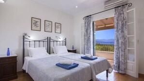 A double bed with white linens, a nightstand with a lamp, and a balcony with patterned curtains. - Villa Ftelias by Villa Plus (Άγιος Στέφανος)