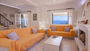 A living room with two orange sofas, a white coffee table, and a fireplace. - Villa Ftelias by Villa Plus (Άγιος Στέφανος)