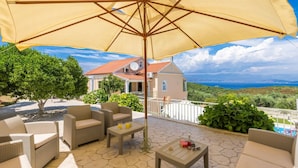 A patio with wicker furniture, a table with drinks, and a large umbrella. - Villa Ftelias by Villa Plus (Άγιος Στέφανος)
