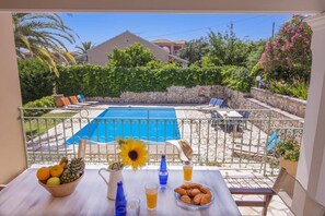 Varanda com vista para uma piscina, uma mesa com frutas, um jarro e copos.