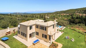 A two-story house with a pool, surrounded by a well-maintained lawn and a scenic view of hills and a distant body of water. - Villa Gina by Villa Plus (Ionian Islands)