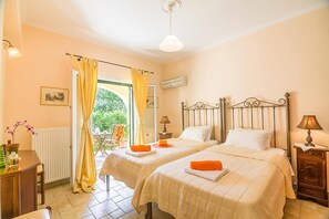 Une chambre avec deux lits, une fenêtre avec des rideaux, un radiateur, un bureau avec une lampe et une petite table avec un vase.