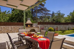 Une terrasse extérieure avec une cheminée en pierre, une table à manger pour deux personnes et une piscine en arrière-plan.