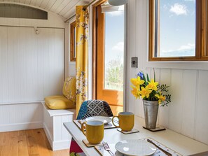 A cozy room with a wooden bench, a yellow floral curtain, a vase of yellow flowers, and a window with a view of trees. - Ty Olwyn Bach - UK36418 (Talybont-On-Usk)