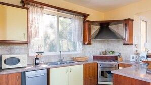 A kitchen with wooden cabinets, a built-in microwave, a sink, and a stove. - Villa Kalliopi by Villa Plus (Kokkini)