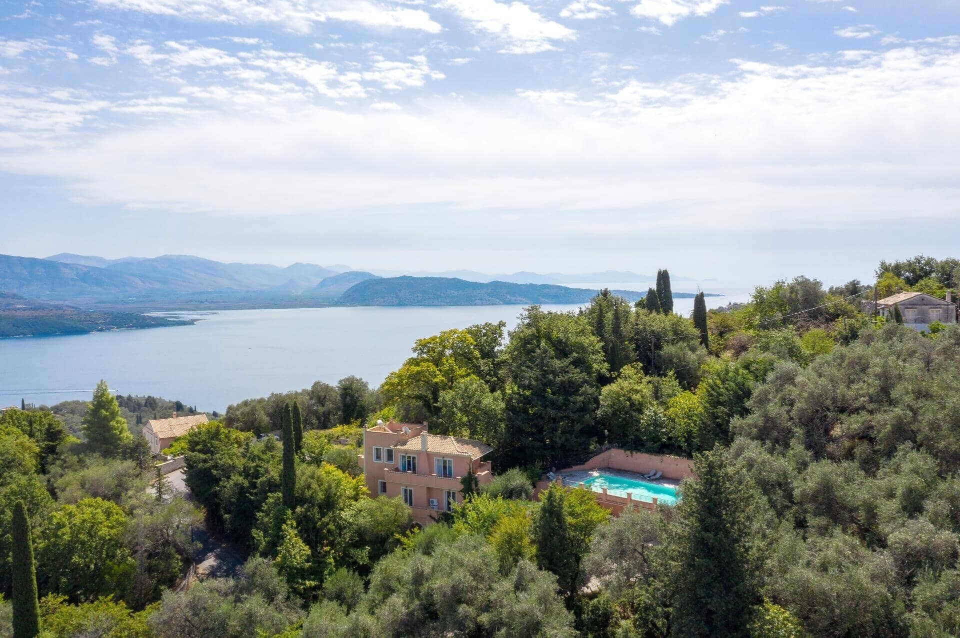 A villa with a swimming pool surrounded by lush greenery and a lake view.