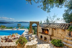 Ein Poolbereich mit Kamin aus Stein, Sitzgelegenheiten im Freien und Blick auf den See.