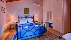 A bedroom with a bed, two bedside tables with lamps, a wardrobe, and an air conditioning unit on the wall. - Villa Kerkyra by Villa Plus (Άγιος Στέφανος)