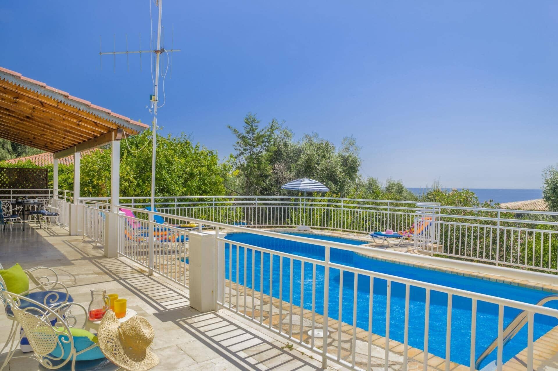 Ein Poolbereich mit Meerblick, eine überdachte Terrasse mit Gartenmöbeln und ein Metallzaun.