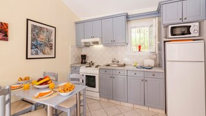 Une cuisine compacte avec des meubles gris, une cuisinière blanche et un four à micro-ondes. On y trouve une table à manger avec des aliments pour le petit-déjeuner et des chaises.