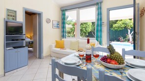 Un coin repas avec une table dressée pour deux personnes, une bouteille de vin et un saladier de fruits.