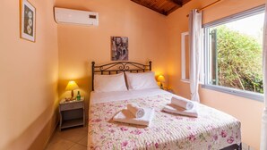 Une chambre à coucher avec un lit, deux lampes de chevet, une fenêtre avec des rideaux, un climatiseur fixé au mur et un tableau encadré.
