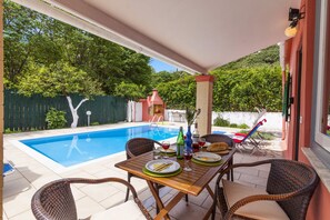 A poolside area with a table set for dining, surrounded by wicker chairs. - Villa Magda by Villa Plus (Άγιος Στέφανος)