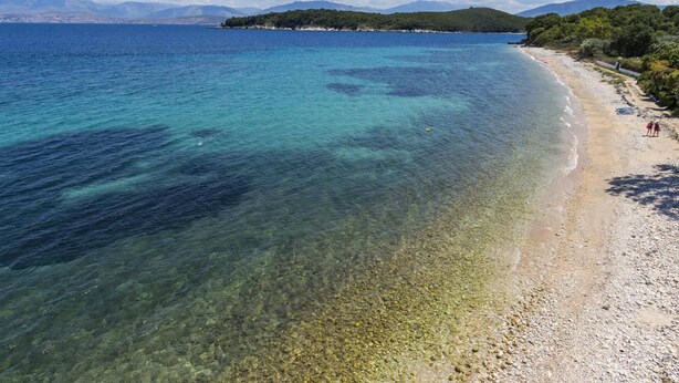 A beach with clear shallow waters, a sandy shore, and a distant mountain range.