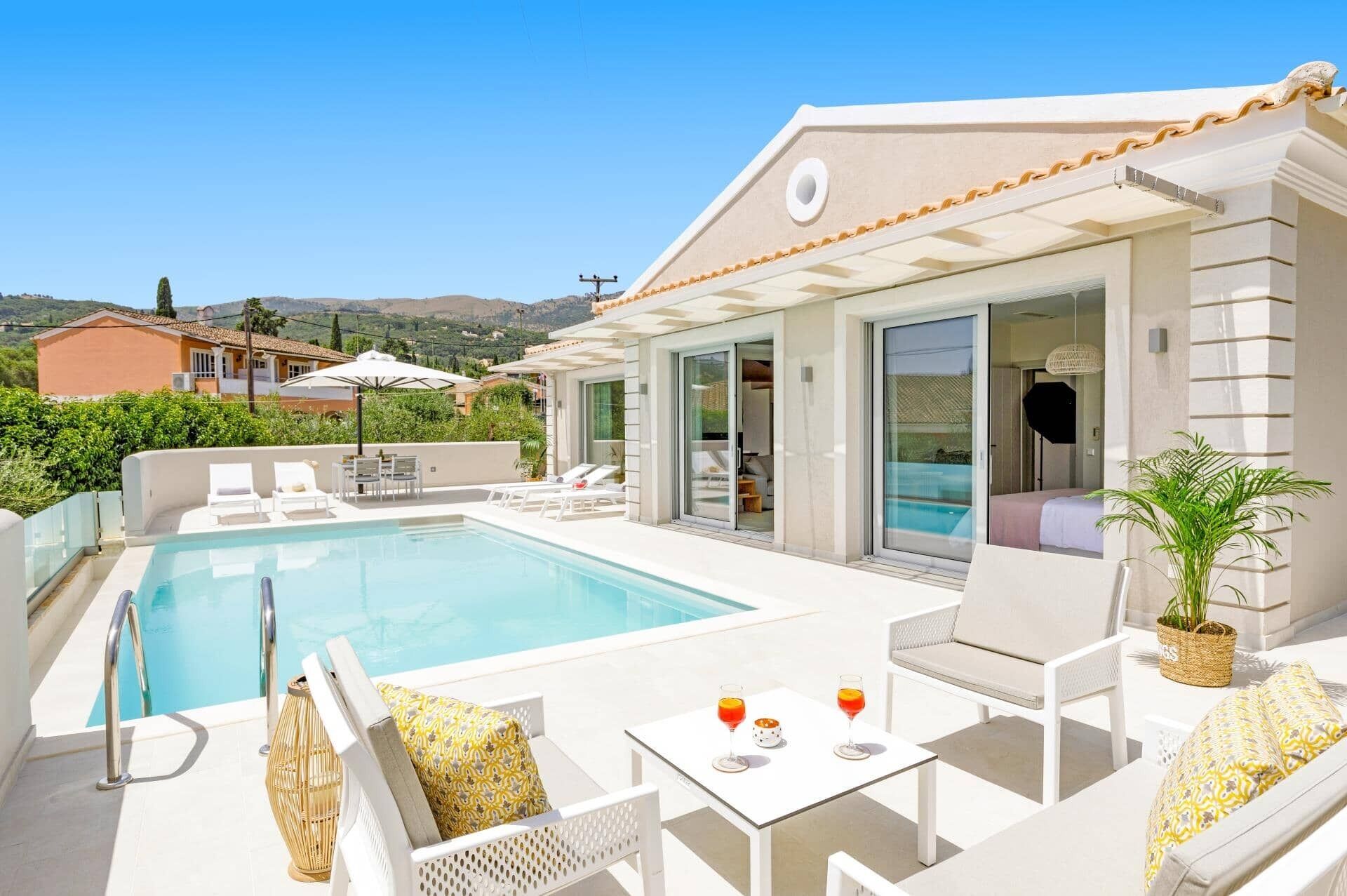 A rooftop pool area with lounge chairs, a table with drinks, and a view of the surrounding landscape.