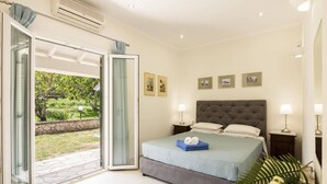 A bedroom with a bed, two bedside tables, a window with curtains, and a view of a garden.