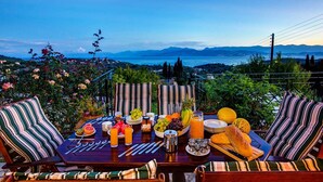 Mesa de jantar posta ao ar livre, com uma vista panorâmica, rodeada por almofadas listradas.