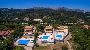 Oversigtsbillede fra luften af tre villaer, Villa Serpa, Villa Petrosa og Villa Carolina, hver med swimmingpool og omgivet af frodig vegetation og bakker.