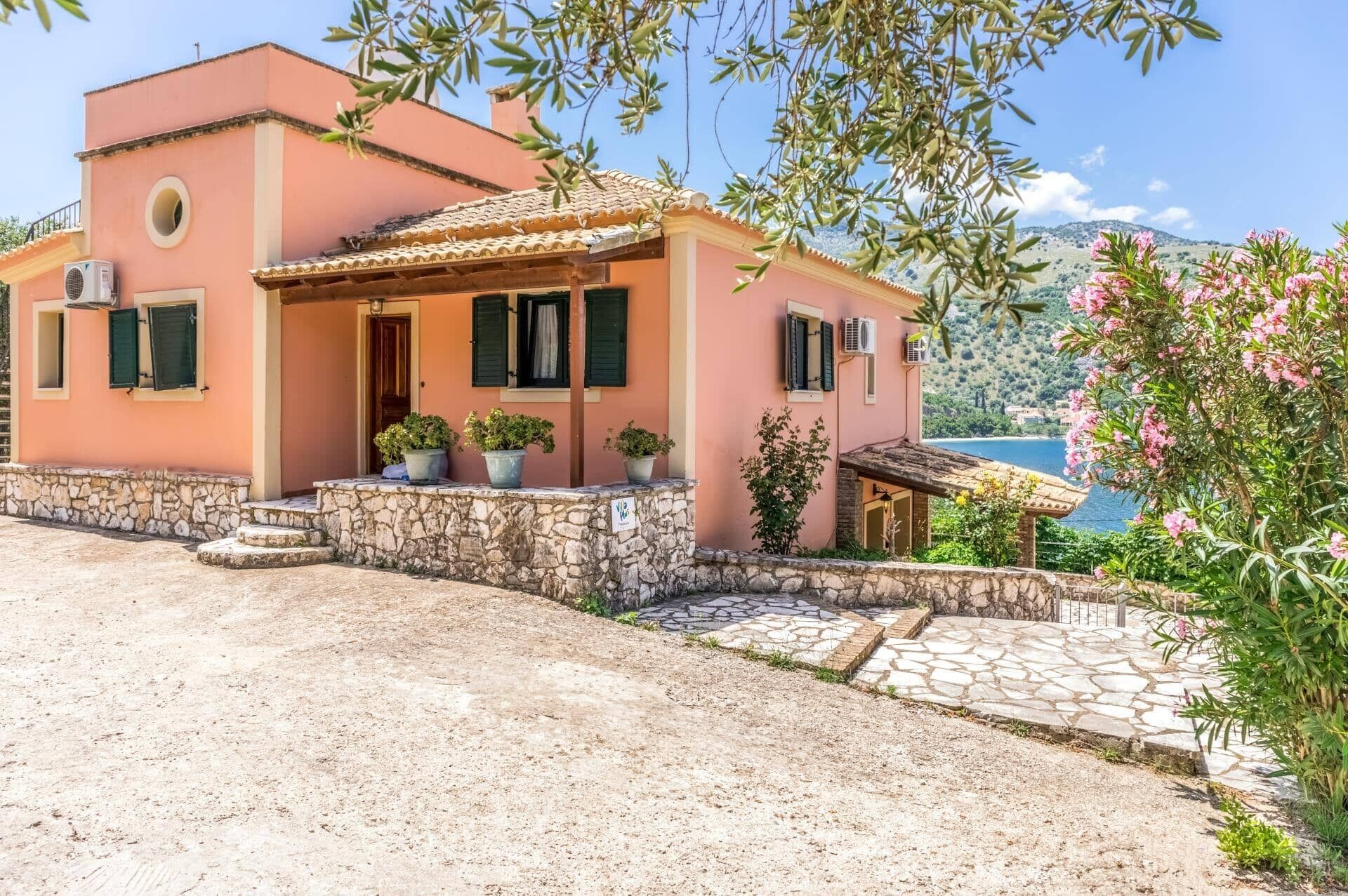 A pink villa with a stone facade, a tiled roof, and a view of the sea.