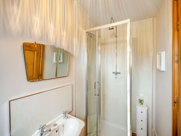 Un baño con cabina de ducha de vidrio, un lavamanos con espejo y un mueble con un objeto pequeño encima.