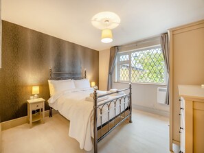 Un dormitorio ordenado con cama de estructura metálica, lámparas de noche, radiador y ventana con vistas.