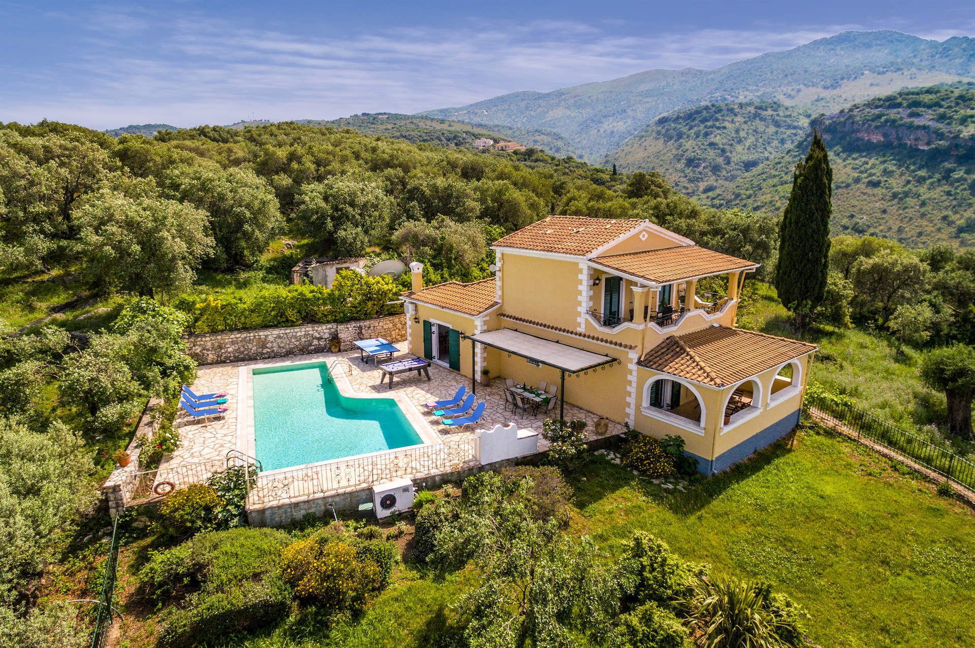 Ein zweistöckiges Haus mit Pool, Sitzgelegenheiten im Freien und Blick auf die umliegenden Hügel.