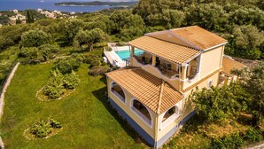 Et toetagers hus med swimmingpool, omgivet af frodig vegetation og udsigt til havet.