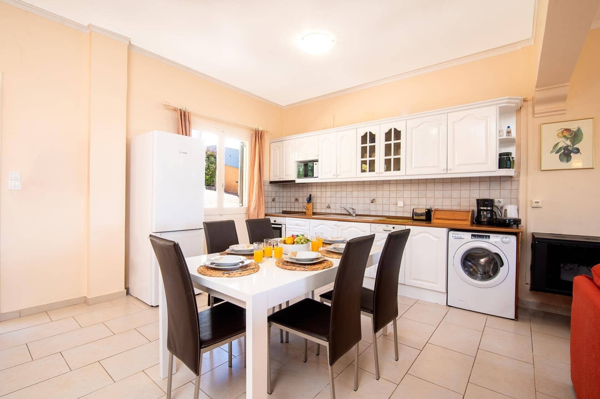 Une cuisine compacte comprenant une table à manger, des chaises, un lave-linge et une machine à café.