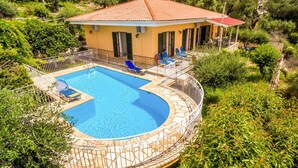 Una villa con piscina, rodeada de vegetación y un edificio de techo rojo.