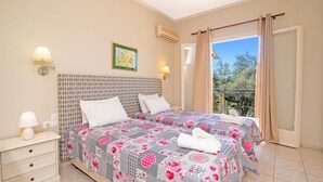 Un dormitorio con dos camas, una mesita de noche, aire acondicionado de pared, un cuadro y un balcón con vistas.