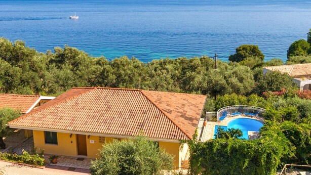 Una propiedad costera con piscina, un edificio amarillo y vista al mar.