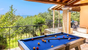 Una mesa de billar con bolas, un área de patio con sillas y vista a zonas verdes.