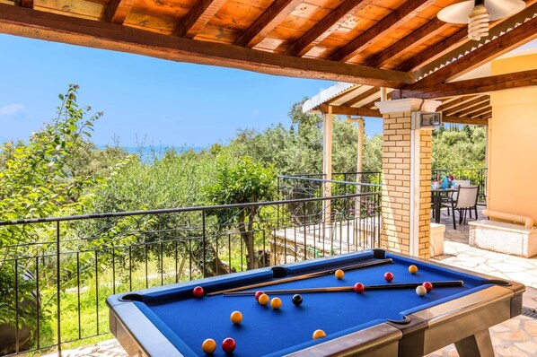 A pool table with balls, a patio area with chairs, and a view of greenery.