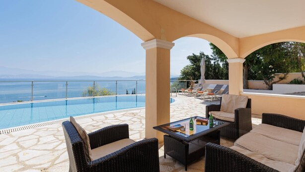Area piscina con mobili in vimini e vista sul mare.
