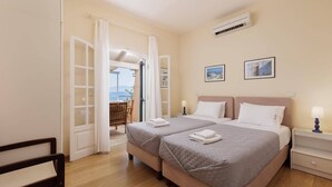 Una camera d'albergo con due letti, una panca di legno, una scrivania e vista mare.