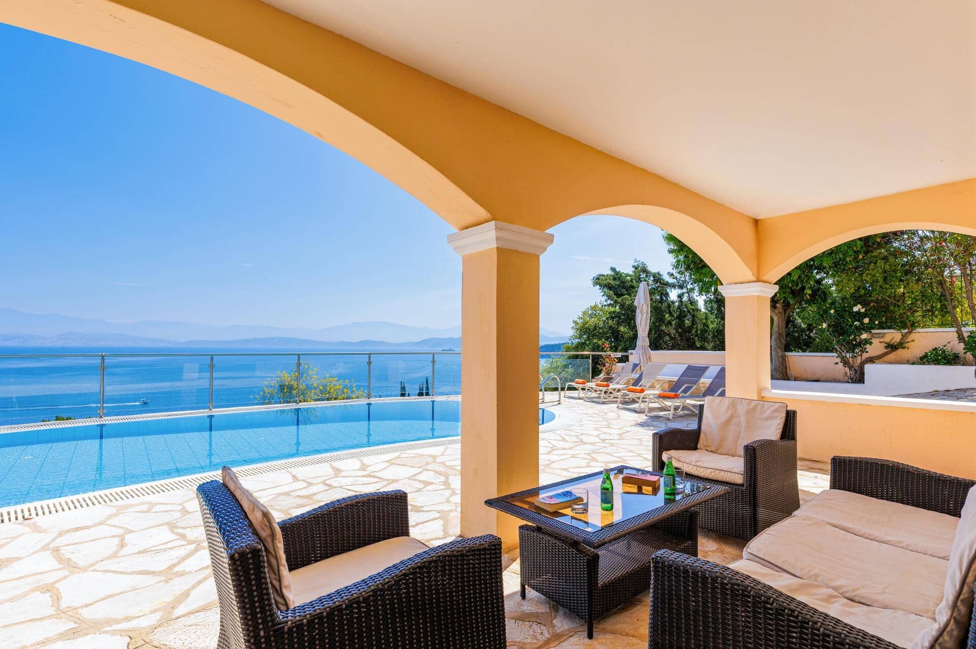 A covered outdoor area with a pool, lounge chairs, and a view of the sea.