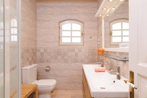 Een badkamer met een toilet, een wastafel met een glazen plank en twee boogvensters.