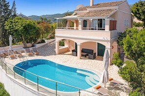 A two-story house with a swimming pool, outdoor seating, and a view of the hills.