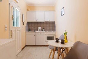 Een kleine keuken met witte kastjes, een kookplaat en een eettafel met stoelen.