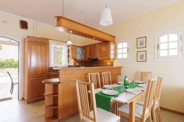 Een moderne keuken met houten kastjes, een centraal eiland en een eethoek met een groene tafelkleed.