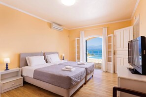A hotel room with two beds, a TV, and a view of the sea.